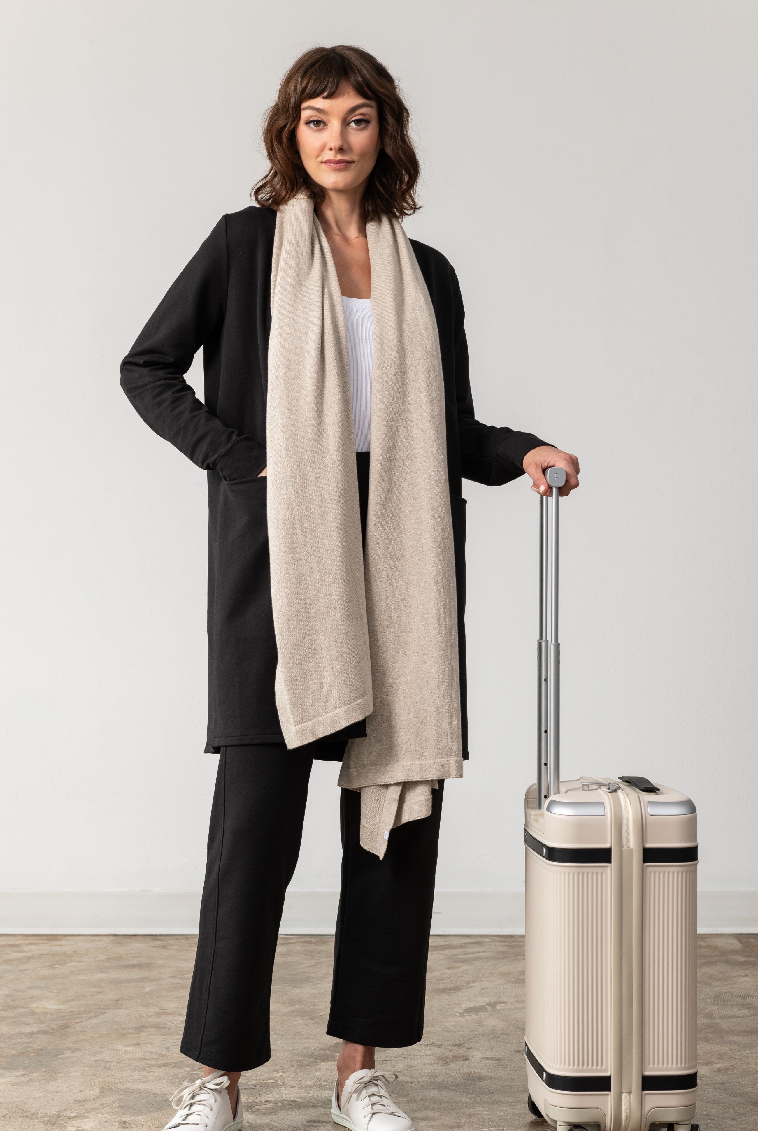 Woman wearing a Beige Scarf draped around her neck and hand on luggage